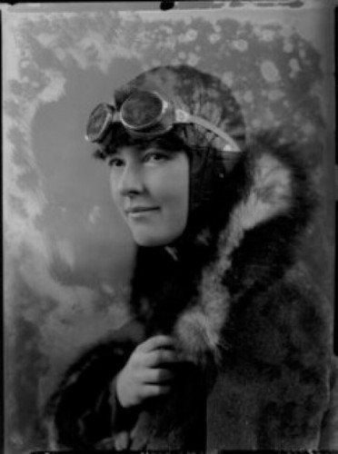 Winifred Brown in black and white head and shoulders photo. 1920s/30s flying outfit fur collar, leather helmet with goggles on forehead. Smiling photo left