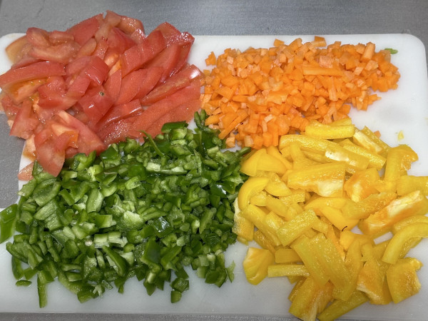 Chopped vegetables including tomatoes, green bell peppers, carrots, and yellow bell peppers on a cutting board.