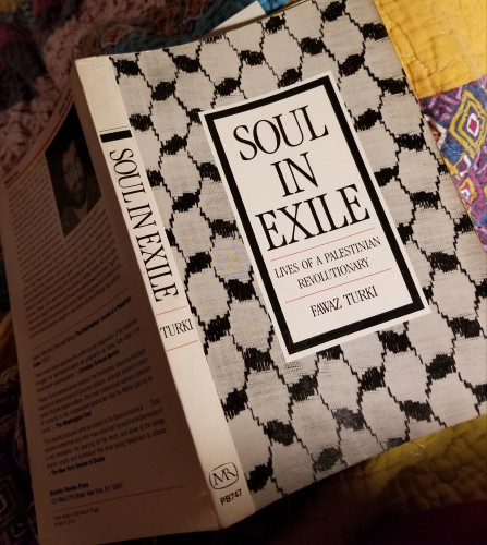 Book, Soul in Exile, by Fawaz Turki. Cover has the fish net pattern of a keffiyeh. The book is open facedown on a quilt.