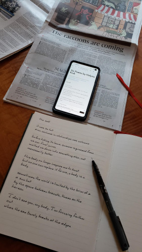 Transcribing the poem "the self" by Halyna Kruk, translated by Ali Kinsella and Dzvinia Orlowsky - the poem is visible on my phone, which is sitting on the Saturday Globe and Mail. My notebook with an uncapped black pen resting on it is just below the phone.