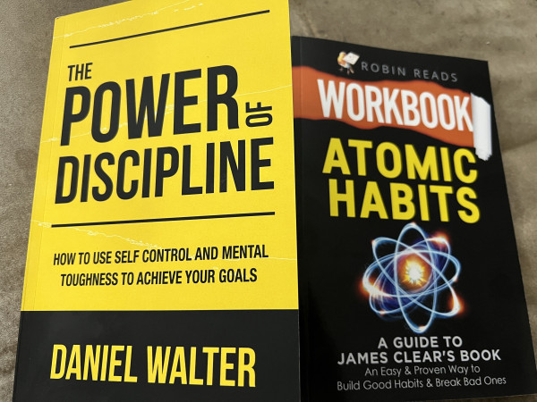 Two books on a surface: "The Power of Discipline" by Daniel Walter and a workbook companion to "Atomic Habits" by James Clear.