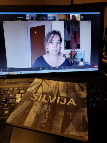 Poet Sandra Ridley on screen, in a zoom book launch for Amanda Earl's Beast Body Epic, reading from some of her own work. In the foreground, Ridley's poetry collection Silvija sits on the computer keyboard.