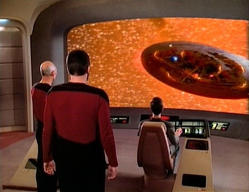 Picture of two Starfleet officers looking at the viewscreen which contains a part of a spacship exploding.