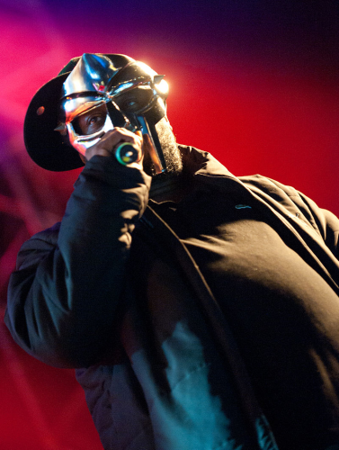 Dutch angle photo of a black man wearing a silver mask holding a microphone