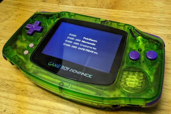 a game boy advance with a custom transparent green shell, purple buttons, and a new ips display. it is sitting on a wooden surface on its back.