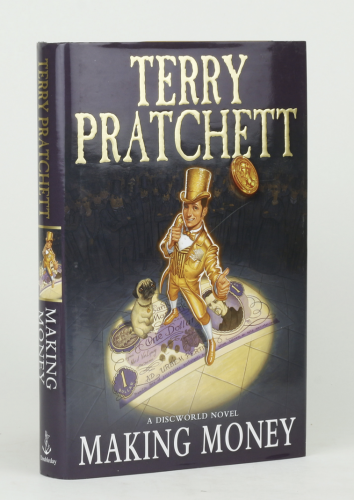 A hard cover copy of Making Money by Terry Pratchett.  It features a man in a golden suit flipping a coin.  A pug is at his feet.