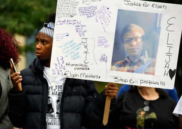 The 2019 photo of Elijah McClain's cousin Rashiaa Veal, shows her standing among the crowd at a press conference holding a sign.  The sign has a picture of Elisha that surrounded by signatures, statements and demands for justice. Some of things written include: "Justice for Elijah", "Humanity Matters – Elijah Matters" and "Stop Evil Protocols!!!!".

Photo by: Andy Cross / The Denver Post via Getty Images (Via NBC News)
