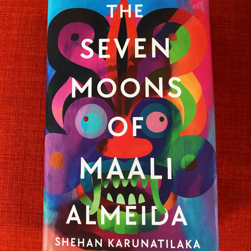The colourful cover pf Secen Moons of Maali Almeida, showing an abstract demonic face in bright colours. 