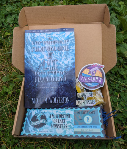 A paperback ARC of A Misfortune of Lake Monsters, a bookmark, two stickers, and a sweet treat in a box.