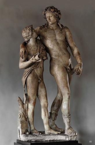 Marble statue group of a drunk Dionysos leaning on a satyr friend. Both hold cups in their hands. Dionysos is in the nude while the satyr is wearing an animal skin over his shoulder, looking adoringly up at the god.