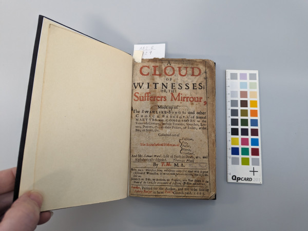 A book with the left board held open. Left endleaf cream machine made paper. 
Title page on right: A cloud of witnesses; or, The sufferers mirrour. Discolouration at edges. Staining in centre.