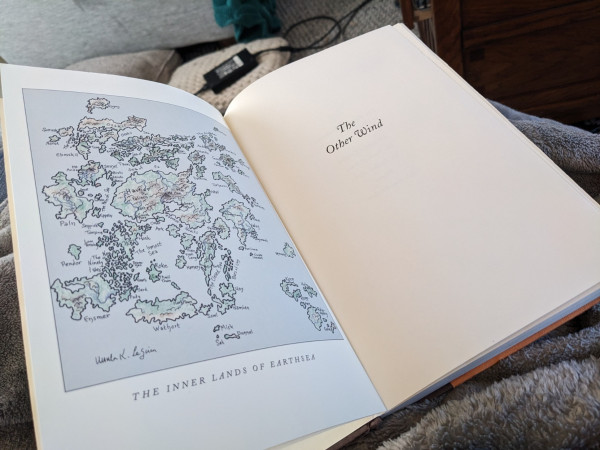 An open book.  The left hand page has a map of Earthsea.  The right hand side is the title page: The Other Wind.
