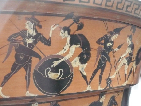 Photograph by me of a red-figure vase painting depicting the Amazons getting ready for battle. The artist used white paint for their skin, a convention to depict women, so it is quite certain that these are women warriors. They are mostly dressed in Phrygian clothes and armour. One of them holds an aspis shield with a kantharos cup on it.