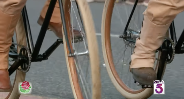 Screencapture from KTLA Channel 5 (Los Angeles) broadcast of the 2024 Rose Parade. Close-up of two vintage bicycles. They are fixed gear with wooden wheel rims and cream-colored tires. The men riding are wearing military buff colors.