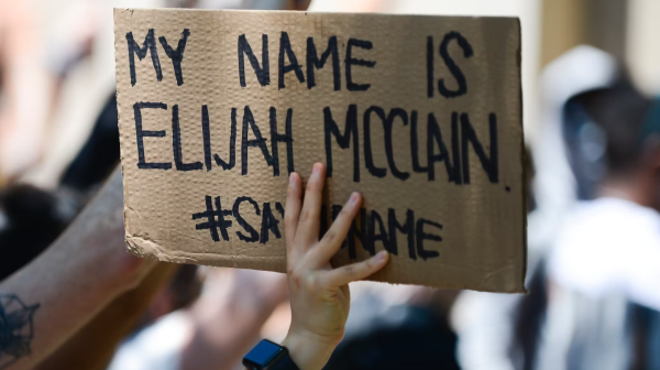 Photograph of a cardboard sign held up by one of many protesters, that reads: "MY NAME IS ELIJAH MCCLAIN. #SayMyName . 
Blurred in the background are a multitude of other protesters.

Photograph from Michael Ciaglo/Getty Images News/Getty Images via mic.com.
