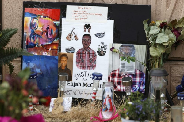 Photograph of a memorial for Elijah McClain, across the street from where the incident occurred. The image shows a multitude of objects placed to remember Elijah. Photographs and drawings of his image are surrounded by flowers, candles, patio lights and other objects..