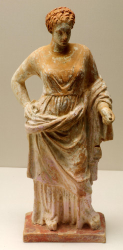 Terracotta statue of the love goddess Aphrodite in a tight-fitting undergarment. The himation is draped around the hips. Her hair is styled in an elegantly braided updo. Traces of pink dye remain on her dress.