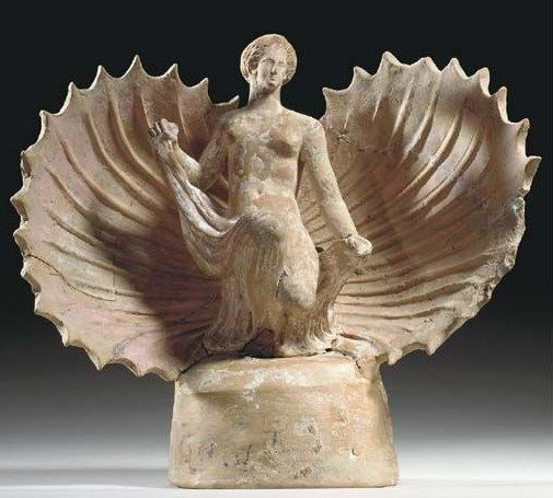 Terracotta figurine of Aphrodite emerging from a seashell. She holds the ends of a fabric in both hands, the bulk of which is draped over her lap.