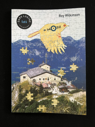 The cover of Dark Lustre, fifth instalment - Roy Wilkinson

Hitler’s eyrie, Berchtesgaden, is shown from above, Alps in the background. An illustrated yellow bird flies above. The whole image is that of a jigsaw puzzle, with some pieces missing.