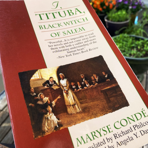 The cover of I, Tituba, Black Witch of Salem by Maryse Condé. A painting of the Salem witch trials with Tituba accused superimposed on dark red and a lighter background