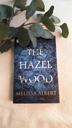 The cover shows the title: The Hazel Wood in white letters intertwined with blue leaves. 
