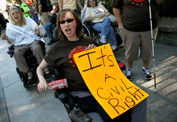 Photo of disability activists protesting subminimum wage regulations. Numerous individuals with disabilities including several wheelchair user's in the forefront of the image, demonstrate as one is holding a sign that reads: "IT'S A CIVIL RIGHT".
