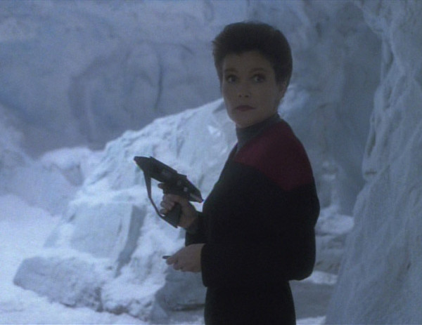 Janeway casually looks over her shoulder while carrying a pistol in an arctic environment.