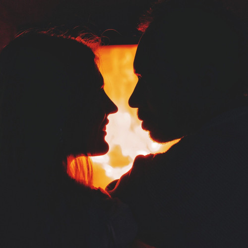 Silhouettes of two people leaning in to kiss. A blurred fire in the background.