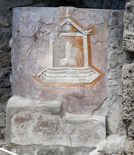 A relief with paint remains depicting a winged phallus seemingly protected by a building with phalluses decorating the outer roof frame.