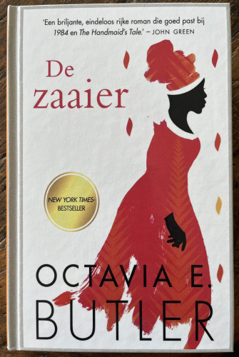 Omslag van het boek "De zaaier" van Octavia E. Butler. Het heeft een silhouet van een vrouw in een rode jurk en hoofdomslag tegen een witte achtergrond, met een citaat van John Green en de sticker "New York Times Bestseller"