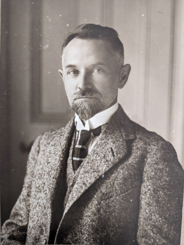 Black and white portrait photograph of a bearded man in a suit and tie