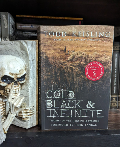 A paperback ARC of COLD, BLACK & INFINITE by Todd Keisling.A large barren landscape with a looking cliff edge. A small well is shown in the desolate field with a child standing there with a figure in black.