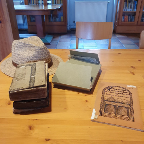 Das Bild zeigt verschiedene alte Bücher und einen Strohhut auf einem Tisch.