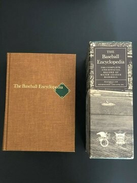 image of the front and the spine of the very thick statistical book The Baseball Encyclopedia from 1969. The is a small green baseball diamond near the right edge of the title test and an image of a ballfield from left field of a ballpark on the spine. The background is dark, and the image is rectangular vertical orientation.